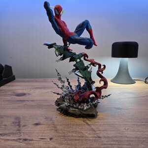 May include: A red and blue Spider-Man action figure is posed in mid-air, swinging from a web. The figure is perched atop a green and gray spaceship with red flames erupting from the base.