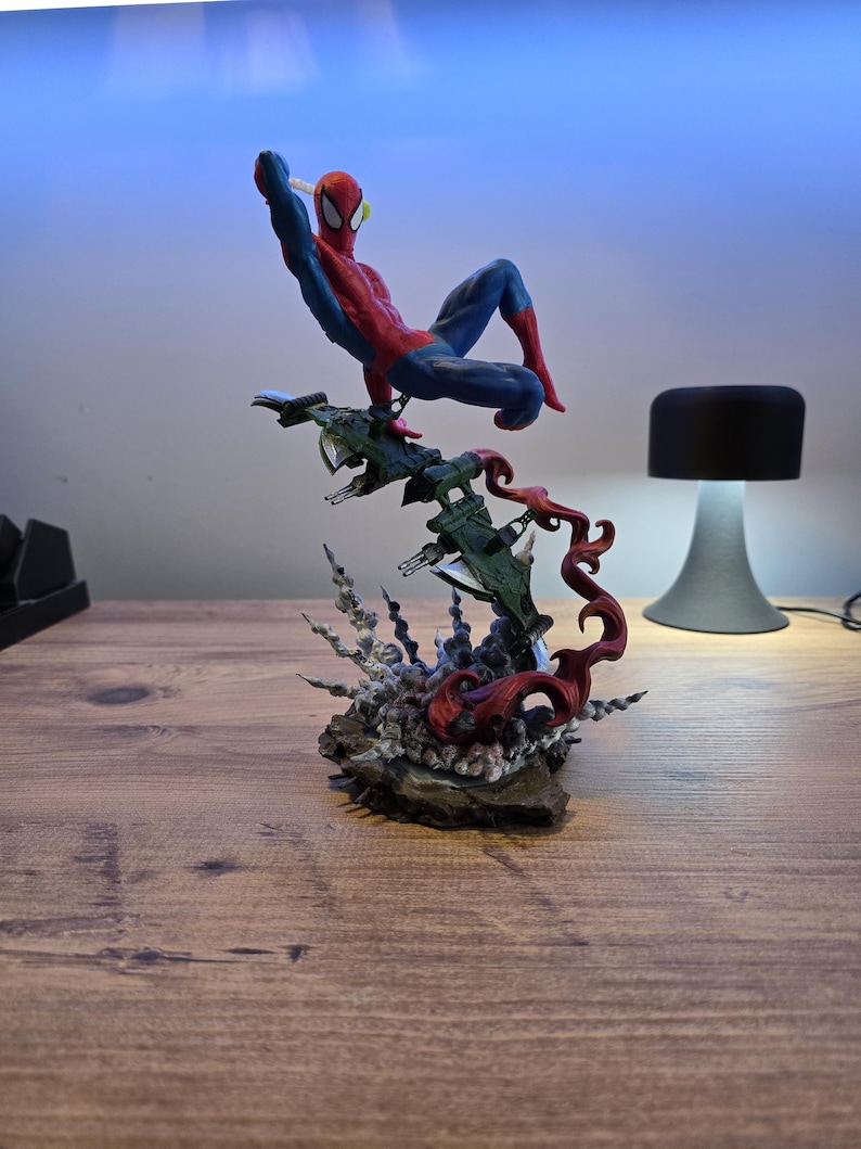 May include: A red and blue Spider-Man action figure is posed in mid-air, swinging from a web. The figure is perched atop a green and gray spaceship with red flames erupting from the base.