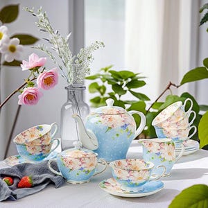 Op de afbeelding: Een blauwe en witte bloemen theeset met een theepot, roomkan, suikerpot en vier theekopjes en schoteltjes. De set heeft een delicaat bloemenpatroon met roze en blauwe bloemen.