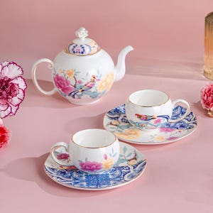 May include: A white porcelain tea set with floral and bird designs. The set includes a teapot, two teacups, and saucers. The cups and saucers have gold rims. The teapot has a decorative lid. The floral design includes pink, yellow, and blue flowers.