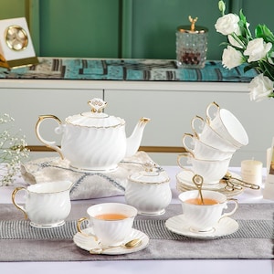 Könnte beinhalten: Weißes Porzellan-Tee-Set mit goldenen Akzenten. Das Set beinhaltet eine Teekanne, eine Zuckerdose, eine Milchkännchen und sechs Teetassen und Untertassen.