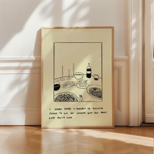 May include: A framed art print featuring a black and white line drawing of a dinner table setting. The illustration includes plates of food, wine glasses, candles, and a wine bottle. Text at the bottom reads: "I know there is probably no definitive purpose to life but dinners with you must come pretty close."