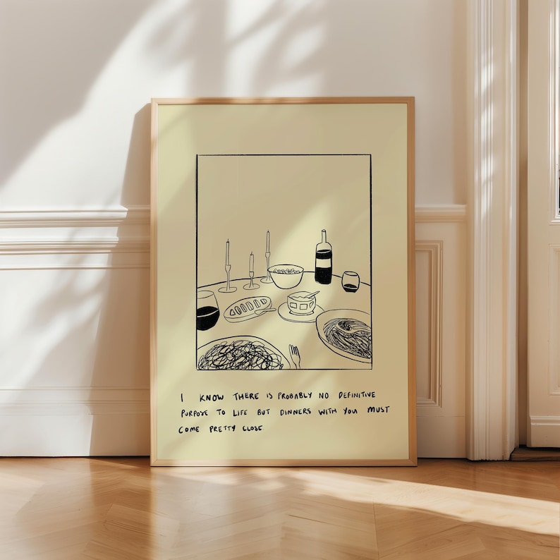 May include: A framed art print featuring a black and white line drawing of a dinner table setting. The illustration includes plates of food, wine glasses, candles, and a wine bottle. Text at the bottom reads: "I know there is probably no definitive purpose to life but dinners with you must come pretty close."