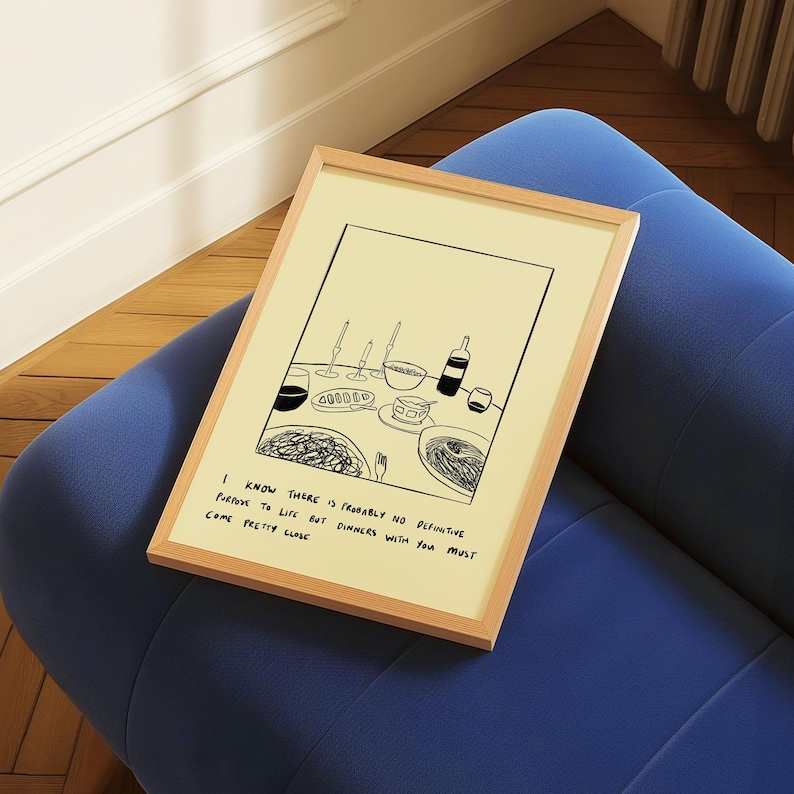 May include: A framed art print featuring a black and white illustration of a dinner table setting with wine glasses, a bottle, and plates of food. The print has a light wood frame and includes the text: "I know there is probably no definitive purpose to life but dinners with you must come pretty close."