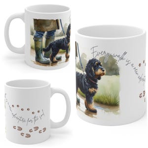 Puede incluir: Taza de cerámica blanca con una ilustración en acuarela de un perro negro y marrón con correa. La taza tiene el texto "Every walk is a new adventure for the soul" y huellas de patas.