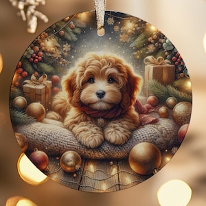 Peut inclure: Ornement de Noël rond représentant un chiot brun clair avec une écharpe rouge, niché sur un coussin en tricot. Le fond comprend des décorations de Noël, des boîtes cadeaux et des boules dorées. Un ruban doré est attaché pour suspendre.