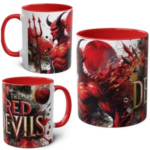 Può includere: Tre tazze in ceramica con interni e manici rossi. Le tazze presentano un'illustrazione di diavolo rosso, un tridente e la scritta "The Red Devils". I disegni sono su sfondo bianco con accenti rossi.