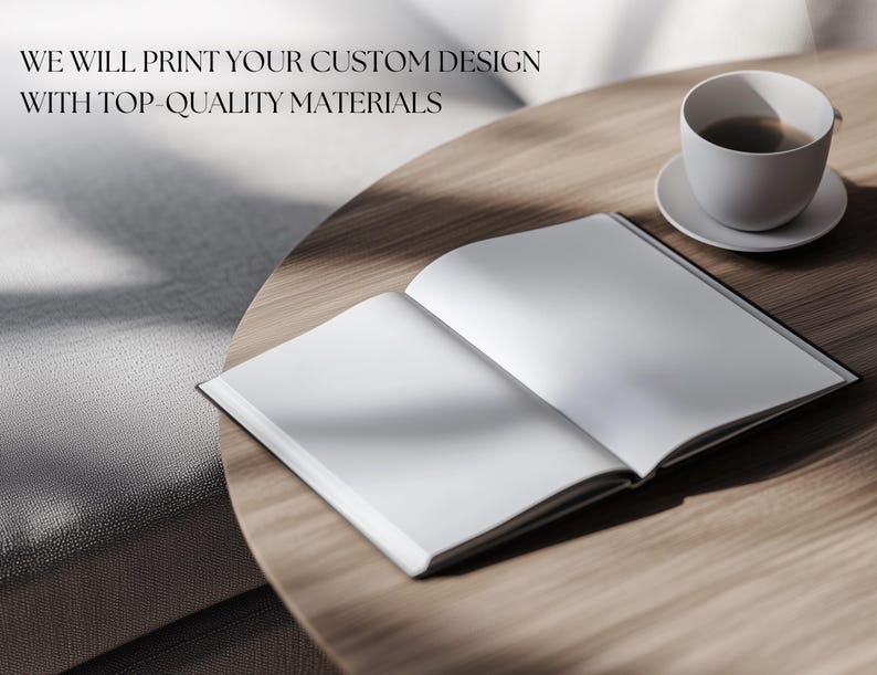May include: A blank, white book with a black spine is open on a wooden table. A white coffee cup with a brown liquid inside is on a white saucer to the right of the book. The text "WE WILL PRINT YOUR CUSTOM DESIGN WITH TOP-QUALITY MATERIALS" is visible at the top of the image.