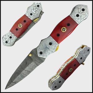 May include: A folding knife with a red handle and a patterned blade. The handle has silver-coloured metal accents with floral designs and gold-coloured details. The blade has a unique, swirling pattern.