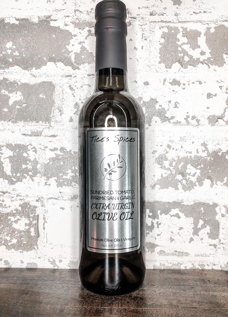 May include: A glass bottle of extra virgin olive oil with a silver label that reads "Tice's Spices Sundried Tomato, Parmesan & Garlic Extra Virgin Olive Oil Premium Olive Oils & Vinegars Net Wt 375ml".