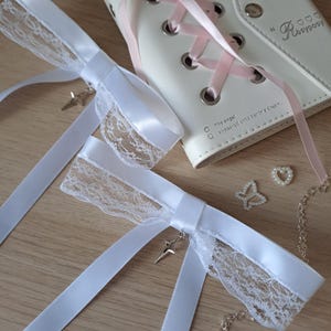 以下が含まれることがあります： 繊細なレーストリムと小さなシルバースターチャームが付いた白いサテンリボン。 リボンは、ピンクのリボンレースと「Rosyposy」のテキストが特徴の白いノートブックと組み合わされています。 パールバタフライとハート型のビーズも存在します。