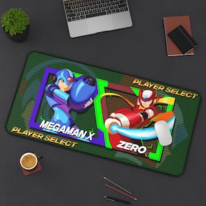 May include: A rectangular green mousepad featuring the characters Megaman X and Zero from the video game series. The mousepad has the text "Player Select" and the character names. A white mouse is on the right side of the pad.