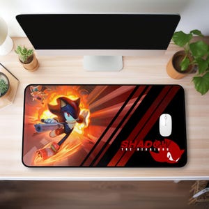 May include: A black and red gaming mouse pad with a graphic of Shadow the Hedgehog from the Sonic the Hedgehog video game series. The graphic features Shadow running with a gun and a red and orange explosion behind him. The text "SHADOW THE HEDGEHOG" is in red and white letters at the bottom of the mouse pad.