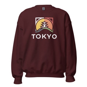Può includere: Felpa color borgogna con una grafica bianca di una pagoda stilizzata davanti a un tramonto con la parola "TOKYO" sotto.