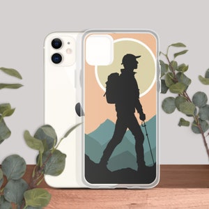 Puede incluir: Una funda transparente para teléfono con la silueta de un excursionista con una mochila caminando por un sendero de montaña. El fondo es de color melocotón con un círculo blanco y montañas azules.