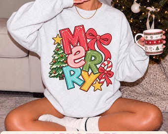 Pode incluir: Uma camisola de gola redonda cor de cinza com uma grande impressão gráfica que soletra a palavra MERRY em letras coloridas e estilizadas. O design inclui uma árvore de Natal verde, um laço vermelho, um bastão de rebuçado e estrelas amarelas.