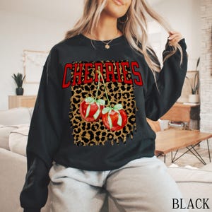 May include: Black sweatshirt with a leopard print design and the word "CHERRIES" in red letters. Two red cherries with green stems and leaves are on the leopard print.
