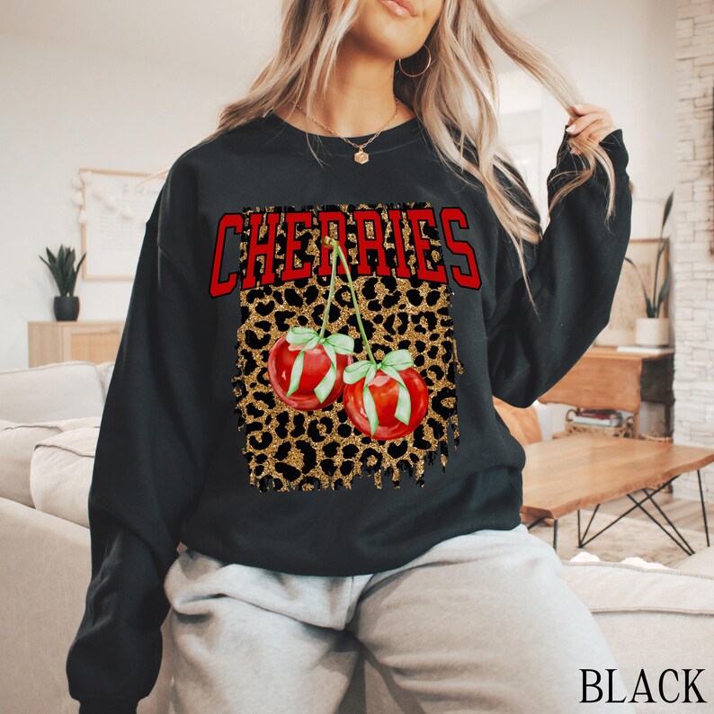 May include: Black sweatshirt with a leopard print design and the word "CHERRIES" in red letters. Two red cherries with green stems and leaves are on the leopard print.