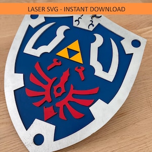 Op de afbeelding: Een blauw, rood, geel en zilver schild met de tekst "LASER SVG - INSTANT DOWNLOAD". Het schild heeft een rood embleem, een gele driehoek en zilveren accenten. Een populair item in de videogame community.