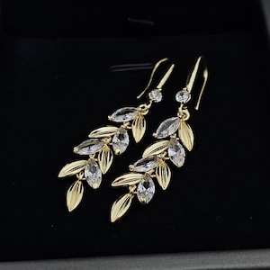 May include: A pair of gold dangle earrings with clear crystal stones set in leaf shapes. The earrings are long and delicate.