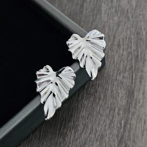 May include: A pair of silver leaf-shaped earrings. The earrings are made of metal and have a textured surface.