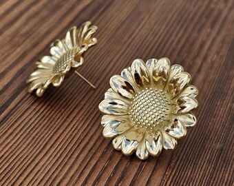 May include: A pair of gold sunflower earrings. The earrings are made of metal and feature a detailed sunflower design.