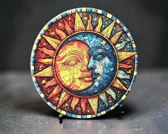 May include: A circular decorative plaque featuring a mosaic-style design of a sun and moon face. The sun is rendered in warm yellow and red tones, while the moon is depicted in cool blue shades. The artwork includes sharp, angular rays.