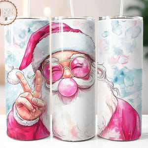 May include: A pink and white watercolor design of Santa Claus wearing pink sunglasses and blowing a bubble. He is giving the peace sign with his left hand. The design is on a stainless steel tumbler.