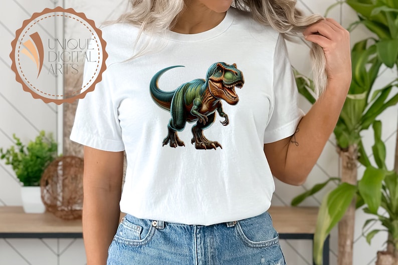 May include: A white t-shirt with a green and blue dinosaur graphic. The dinosaur is facing forward with its mouth open and has a fierce expression.