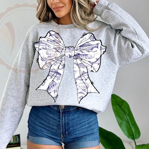May include: A gray sweatshirt with a large white bow printed on the front. The bow is filled with a pattern of small blue fish.
