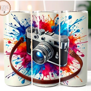 Peut inclure: Un appareil photo vintage avec une sangle en cuir marron est entouré d'éclaboussures de peinture colorées sur un fond blanc. L'appareil photo a un objectif bleu et un corps argenté.