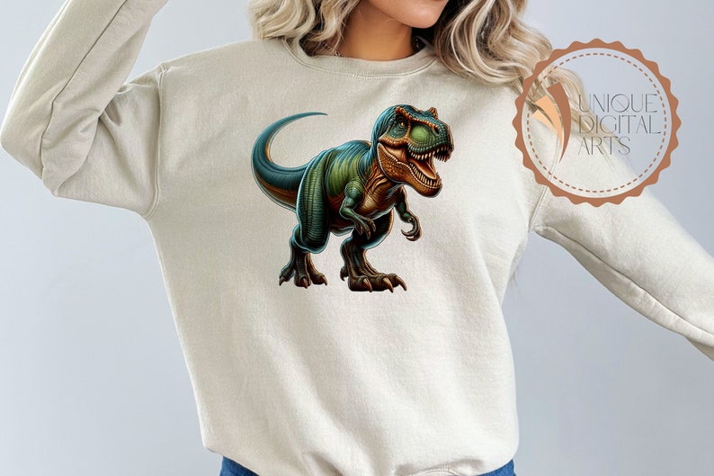 May include: A beige sweatshirt with a green and brown dinosaur graphic on the front. The dinosaur is a Tyrannosaurus Rex with its mouth open and its teeth showing. The dinosaur is facing to the right.