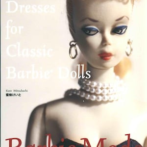 May include: A book cover featuring a Barbie doll with blonde hair, blue eye shadow, and red lipstick. The title reads "Dresses for Classic Barbie Dolls" with Japanese text above. The doll wears a pearl necklace and earrings. The book is a fashion guide.