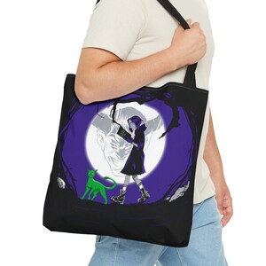 Puede incluir: Una bolsa de tela negra con un diseño morado y blanco que representa a una niña con un gato caminando por un bosque. El diseño incluye una luna llena y árboles.