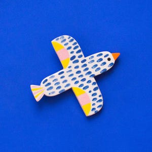 Könnte beinhalten: Ein blauer und weißer Keramikvogel mit gelben und rosa Akzenten. Der Vogel ist mit einem Tupfenmuster bemalt und hat einen kleinen orangefarbenen Schnabel.