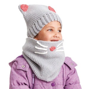Puede incluir: Un conjunto de gorro y braga de cuello de punto gris con diseño de cara de gato. El gorro tiene orejas rosas, y la braga de cuello presenta bigotes blancos y una nariz rosa. El conjunto está diseñado para niños y es de punto suave.