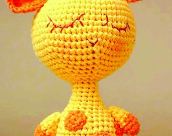 May include: A crocheted giraffe toy with a yellow body and orange spots. The giraffe has closed eyes and a sweet expression.