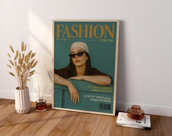 May include: A framed poster featuring a magazine cover titled FASHION, dated June 1987. The cover displays a person wearing a beige beanie and black sunglasses, leaning on a teal surface. Text includes The best SUMMER fashion TRENDS and 10 MUST VISIT luxury shoppes IN PARIS.