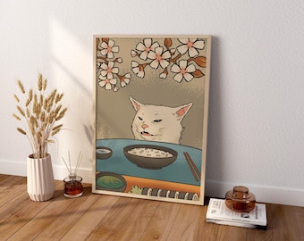 May include: A rectangular framed wall art print featuring a stylized illustration of a white cat with a confused expression sitting at a blue table with a bowl of rice, chopsticks, and sushi, set against a background of cherry blossoms.