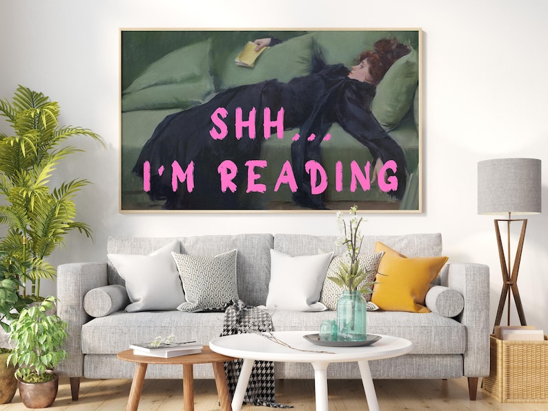 Op de afbeelding: Een schilderij van een vrouw die op een bank ligt en een boek leest. De tekst "Shh... I'm reading" staat in roze letters op het schilderij.