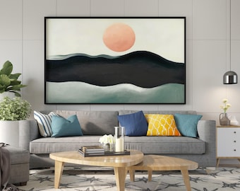 May include: A rectangular wall art print in a black frame featuring a landscape illustration with a large peach-colored sun above dark black rolling hills and a light green foreground, displayed above a gray sofa with colorful throw pillows.