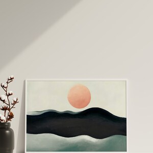 May include: A framed abstract painting with a large, peach-colored circle in the center, representing the sun, above a series of dark blue and green hills.