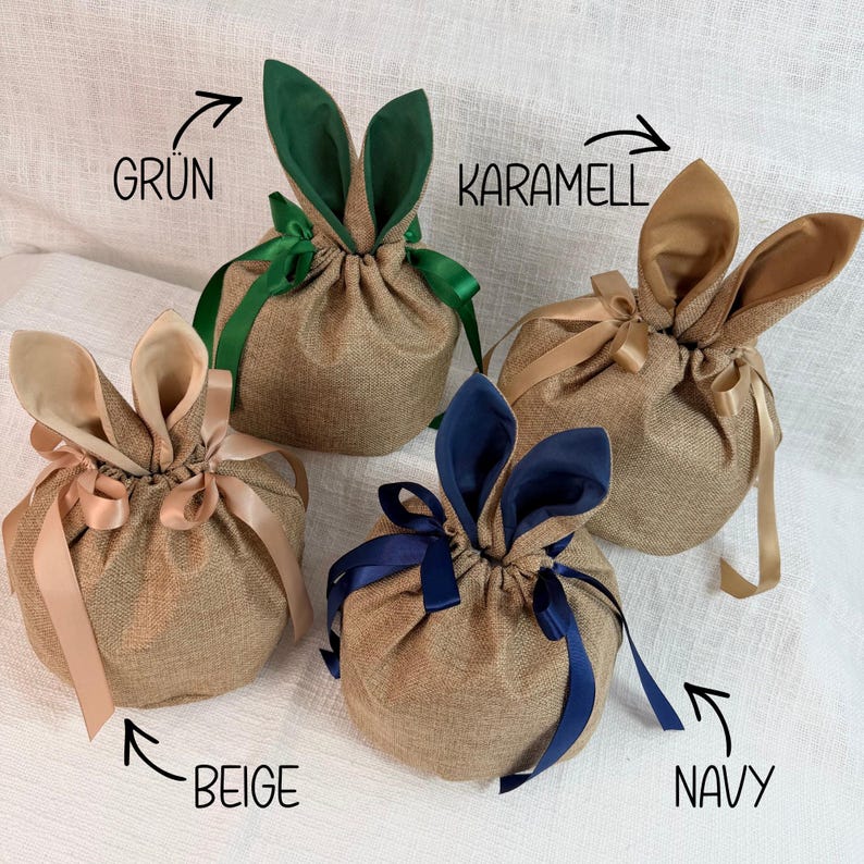 May include: Four burlap gift bags with bunny ear accents. Each bag is a different color: green, caramel, beige, and navy. The bags are tied with matching ribbons and are suitable for Easter or spring gifting.