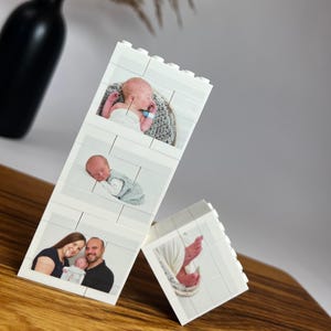 Peut inclure: Blocs blancs de style Lego affichant des photos de b&eacute;b&eacute;. Un bloc montre un b&eacute;b&eacute; dans un panier, un autre montre un b&eacute;b&eacute; endormi et un troisi&egrave;me montre une famille avec un b&eacute;b&eacute;. Un quatri&egrave;me bloc montre les pieds d'un b&eacute;b&eacute;.