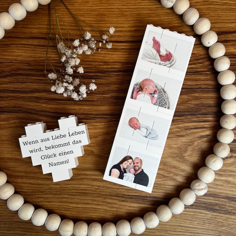 Peut inclure: Un bloc en forme de c&oelig;ur en bois avec le texte "Wenn aus Liebe Leben wird, bekommt das Gl&uuml;ck einen Namen !" &agrave; c&ocirc;t&eacute; d'une bande photo d'un nouveau-n&eacute;. La bande photo montre les pieds, le visage du b&eacute;b&eacute; et une photo des parents.