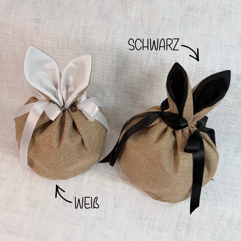 May include: Two burlap Easter bunny-shaped gift bags. One has white ears and a white ribbon, the other has black ears and a black ribbon. The word "SCHWARZ" is written above the black-eared bag, and "WEIB" is written below the white-eared bag.