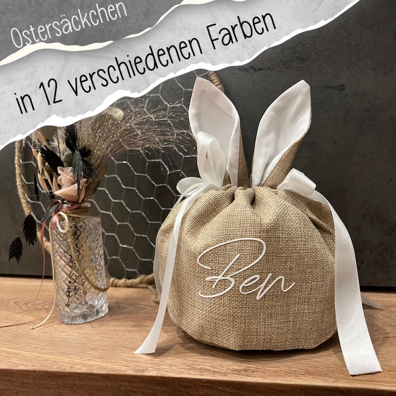 May include: A burlap Easter gift bag with white bunny ears and a white ribbon drawstring. The bag has the name "Ben" in white script. The text "Osters&auml;ckchen in 12 verschiedenen Farben" is in the background.