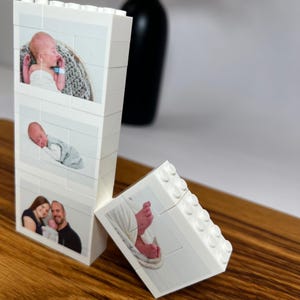 Peut inclure: Des blocs de construction blancs avec des photos d'un nouveau-n&eacute; et de ses parents. Les blocs sont dispos&eacute;s sur une surface en bois, avec un vase noir en arri&egrave;re-plan. Les photos sont imprim&eacute;es sur les blocs.