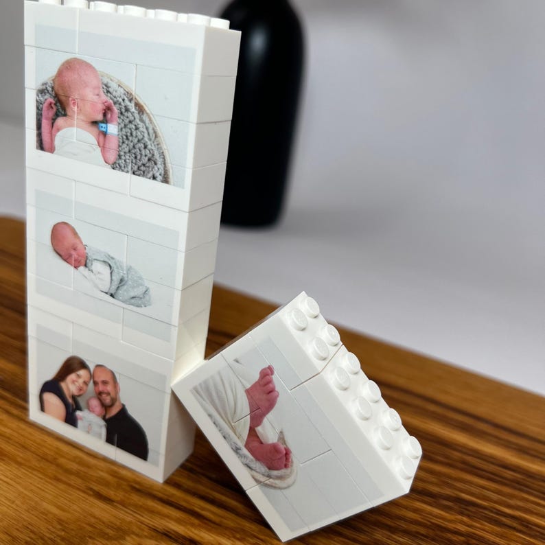 Peut inclure: Des blocs de construction blancs avec des photos d'un nouveau-n&eacute; et de ses parents. Les blocs sont dispos&eacute;s sur une surface en bois, avec un vase noir en arri&egrave;re-plan. Les photos sont imprim&eacute;es sur les blocs.
