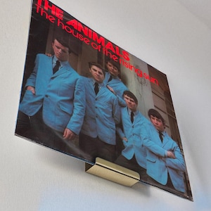 May include: Album cover for The Animals' "The House of the Rising Sun" featuring the band in light blue suits. The album is displayed on a wall-mounted holder above a stereo system.